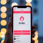 Um smartphone com o aplicativo Tinder aberto na tela, mostrando o familiar logo de chama e potenciais matches.