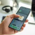 Uma mão segurando um smartphone com a bandeja do chip parcialmente ejetada, mostrando o aplicativo WhatsApp aberto na tela.