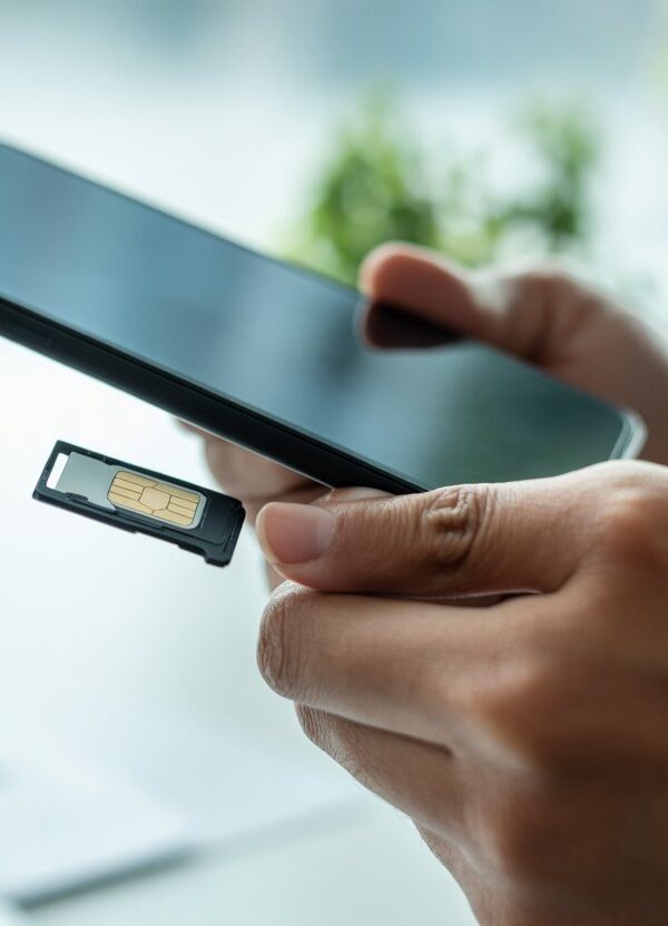 Pessoa segurando um smartphone com o compartimento do chip parcialmente aberto, em um ambiente de escritório claro.